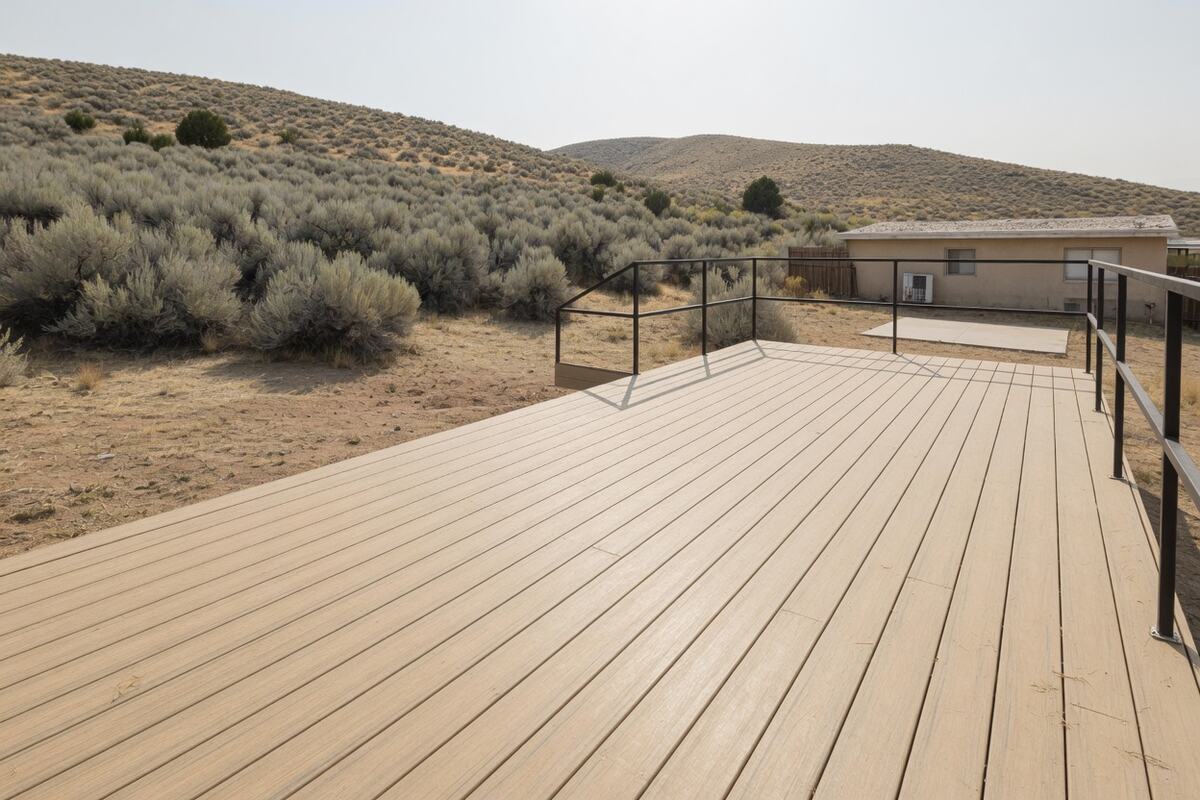 Light tan composite deck boards and a dark metal rail in hard sun, with dry hills behind.